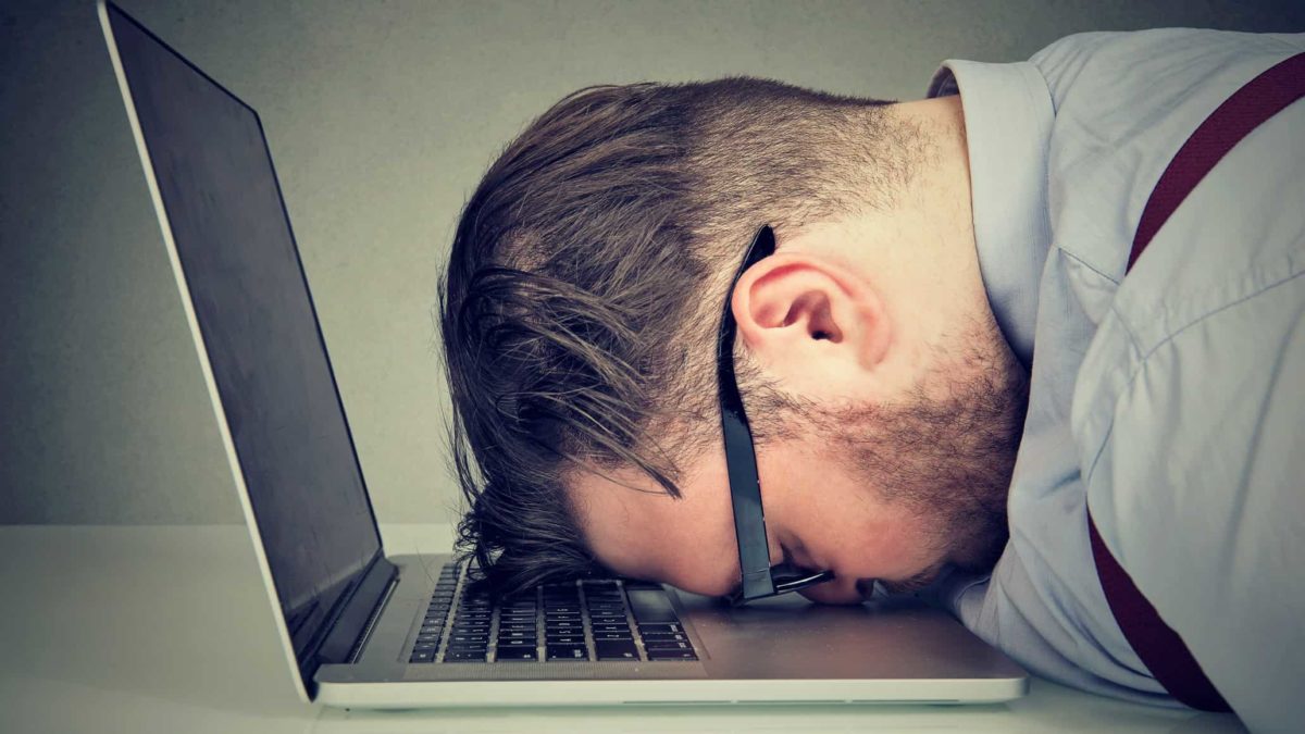 Side-on view of a devastated male investor laying his head on his laptop keyboard