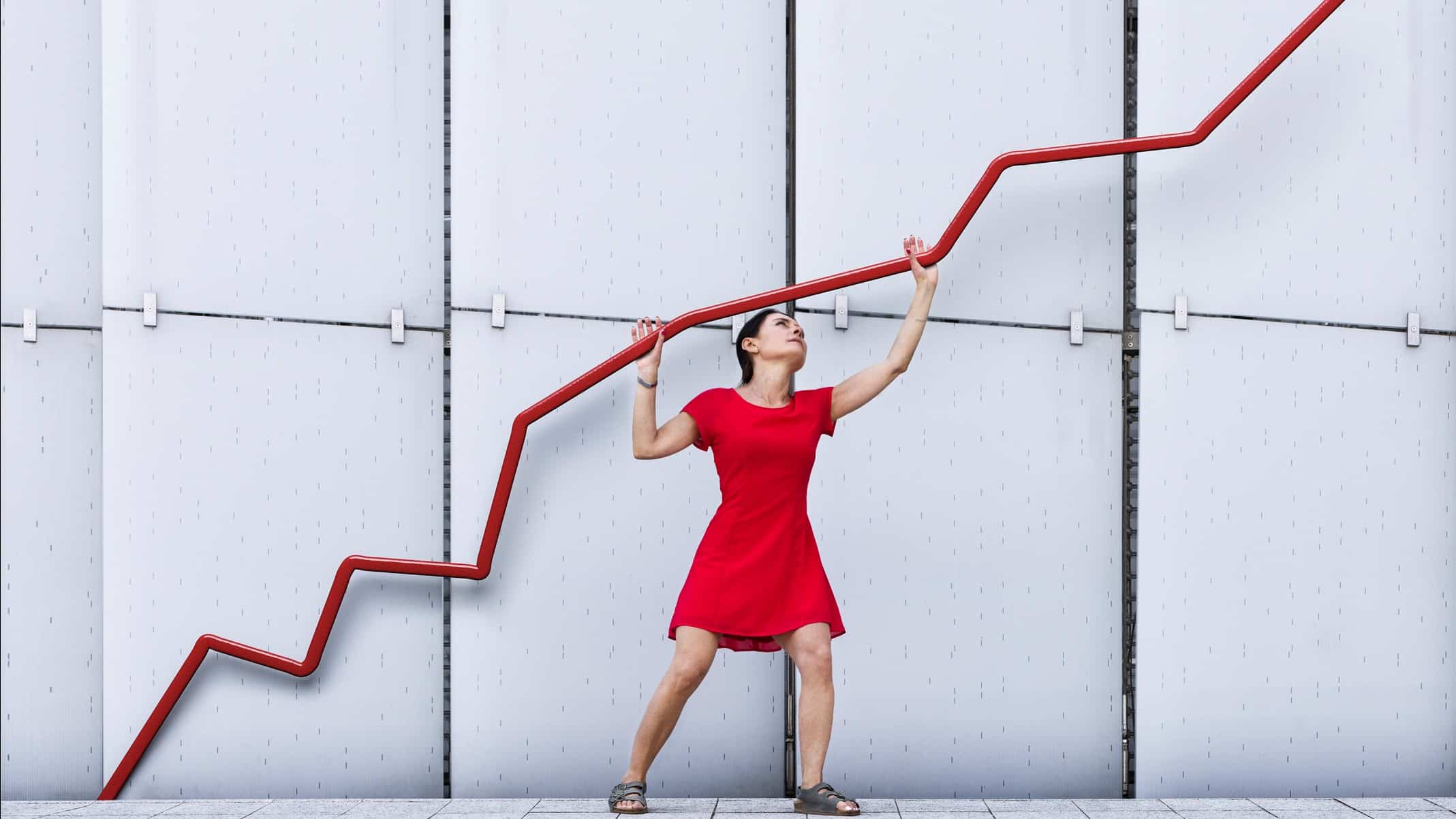 A woman in a red dress holding up a red graph.