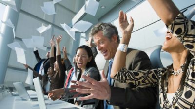 A group of happy office workers throw papers in the air and cheer.