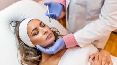 A woman lies down with eyes closed as she prepares to receive a cosmetic injectable in her face.