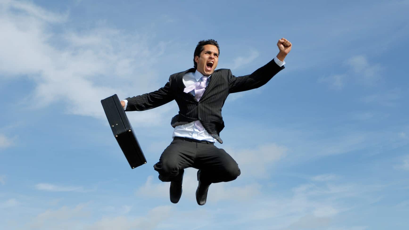 Businessman in suit and holding a briefcase jumps into the sky celebrating the rising share price.