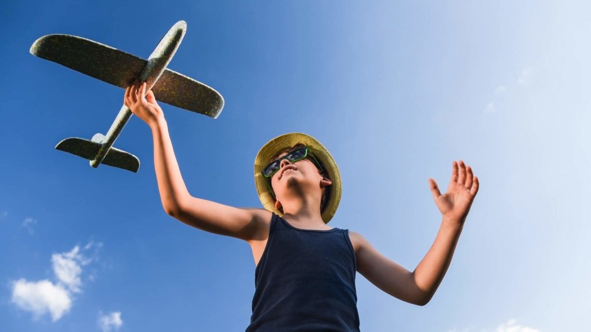 Teenager holds model plane in the air against the background of a blue sky.