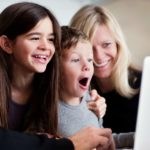 Family smile and laugh as they look at a laptop.
