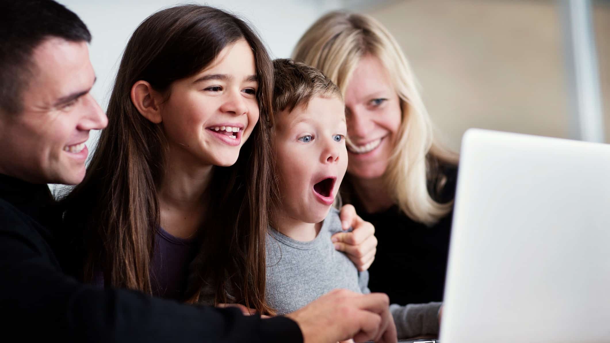 Family smile and laugh as they look at a laptop.