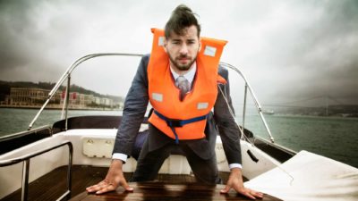 A business man wearing a life jacket prepares to jump off a sinking boat