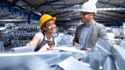 Factory worker wearing hardhat and uniform showing new metal products to the manager supervisor.