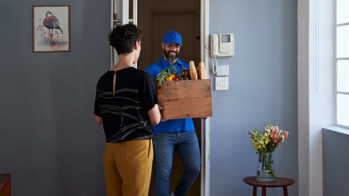 A delivery man carries a basket of food into an apartment
