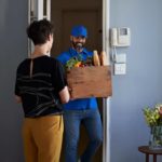 A delivery man carries a basket of food into an apartment