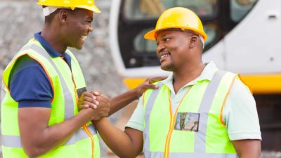 Two cheerful miners shake hands while wearing hi-vis and hard hats celebrating the commencement of a HAstings Technology Metals mine and the impact on its share price