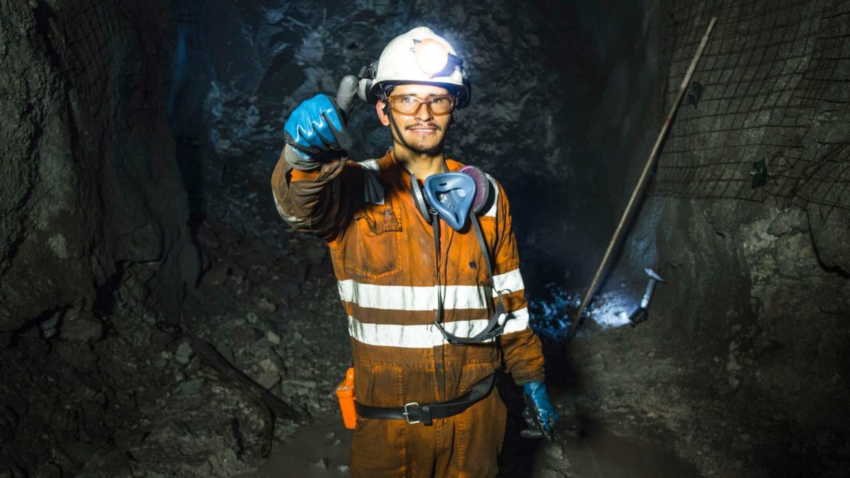 A uniformed Peninsula Energy miner standing inside a black mine raises his hand in a thumbs up motion