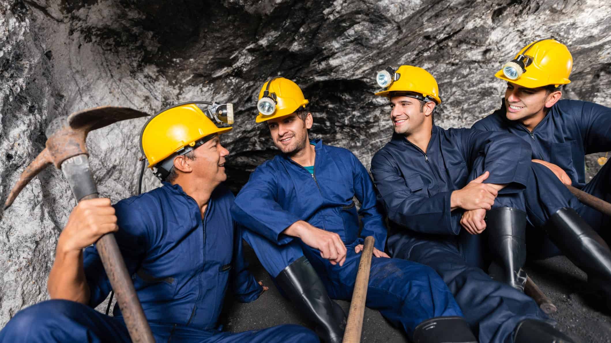 A group of miners in hard hats sitting in a mine chatting on break