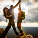 Two hikers high five each other having climbed to the top pinnacle of the mountain.