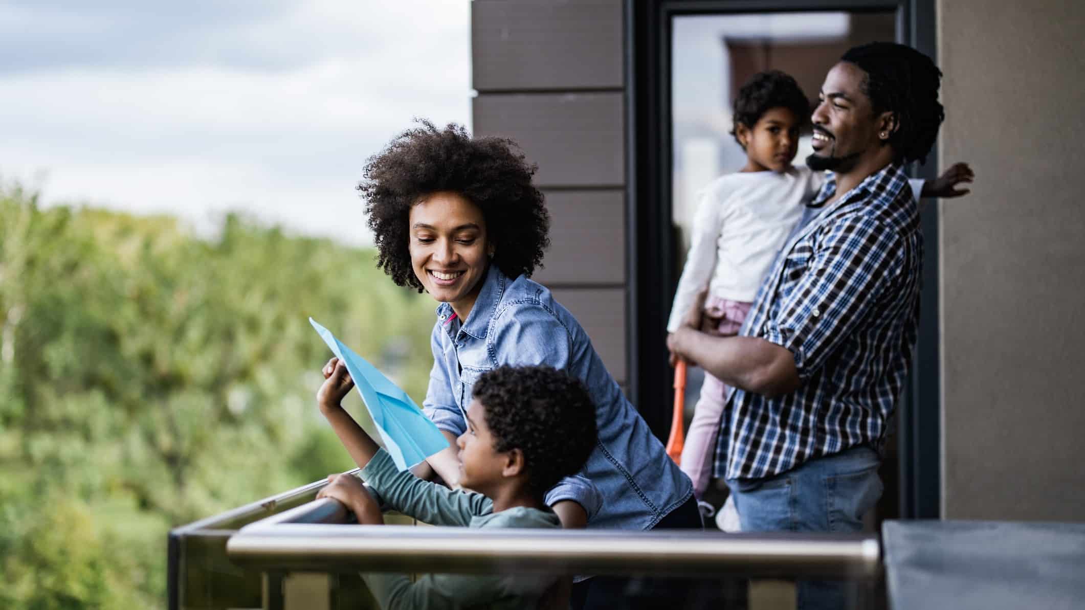 A young family with two kids smiling as they stand on the balcony of an apartment they are inspecting after seeing it advertised on REA