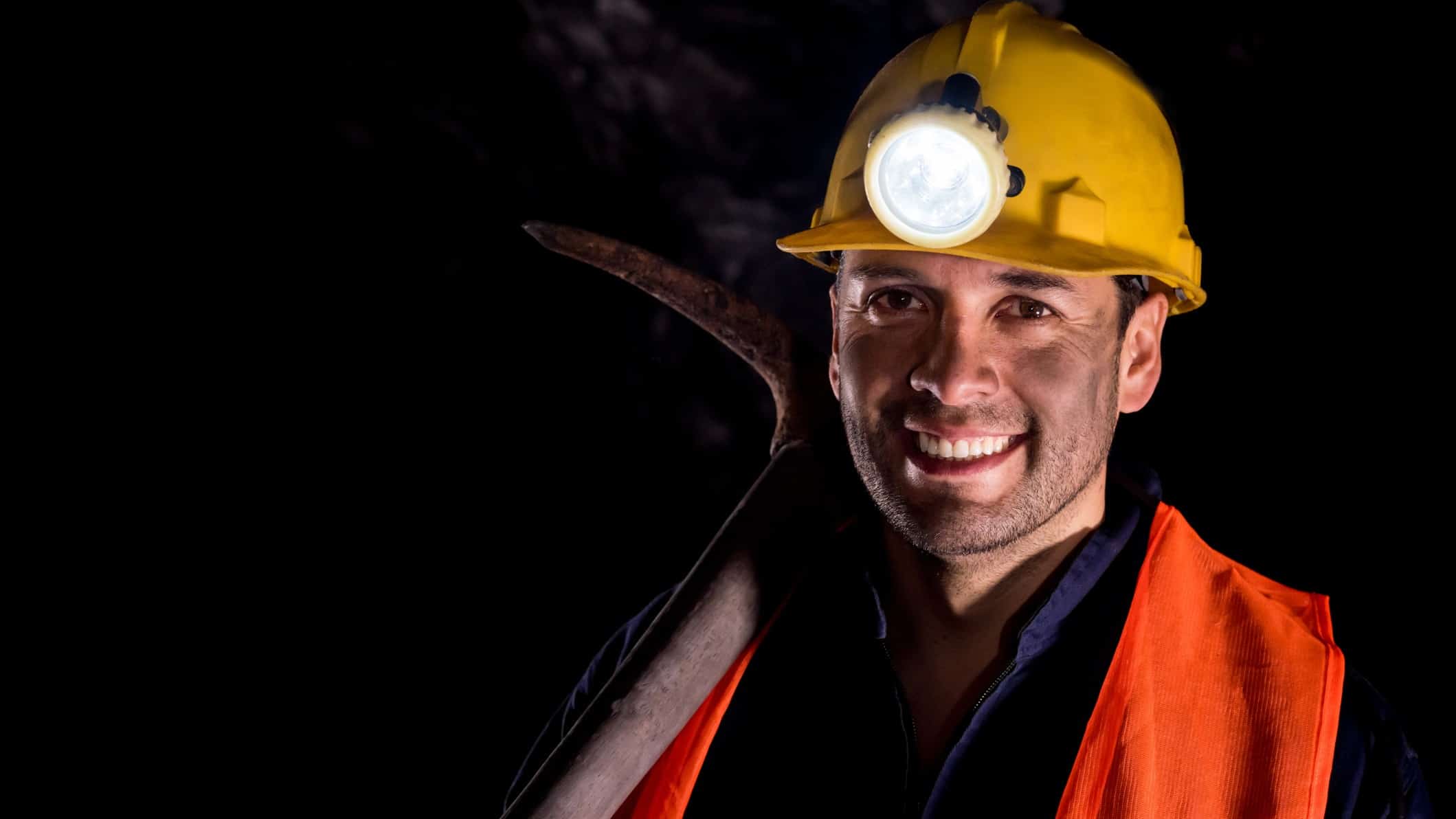 Happy man mining and wearing a helmet in a dark mine underground.