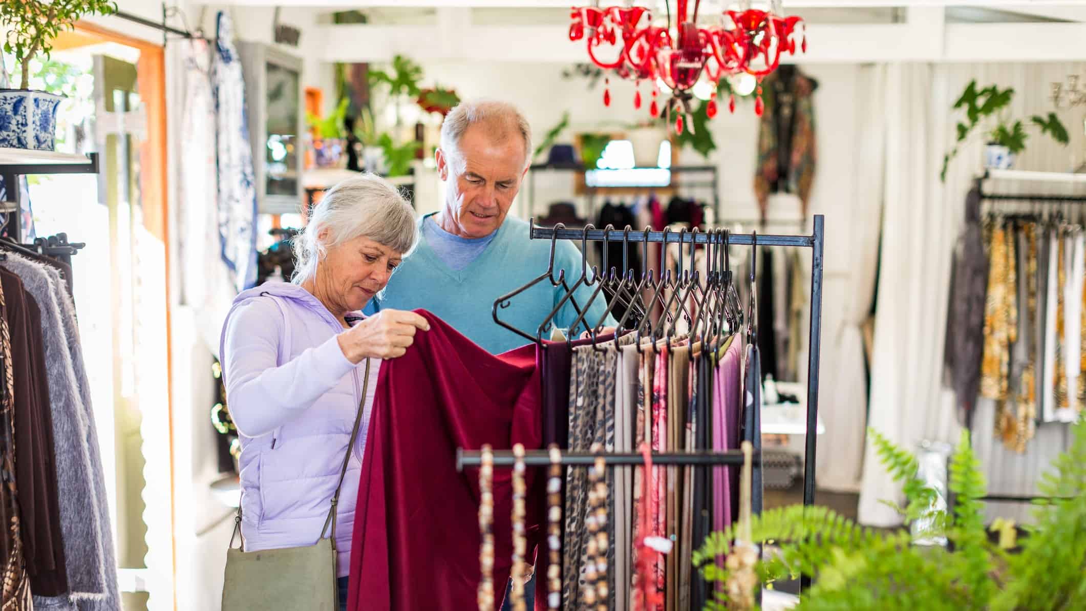 A middle aged couple look at clothing on a rack in a retail store