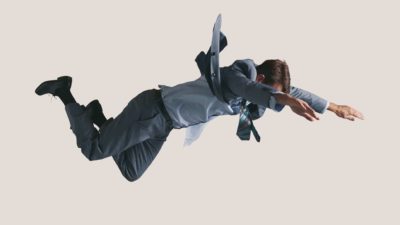 A man in a business suit hangs in mid air facing the floor as he plunges to the ground.