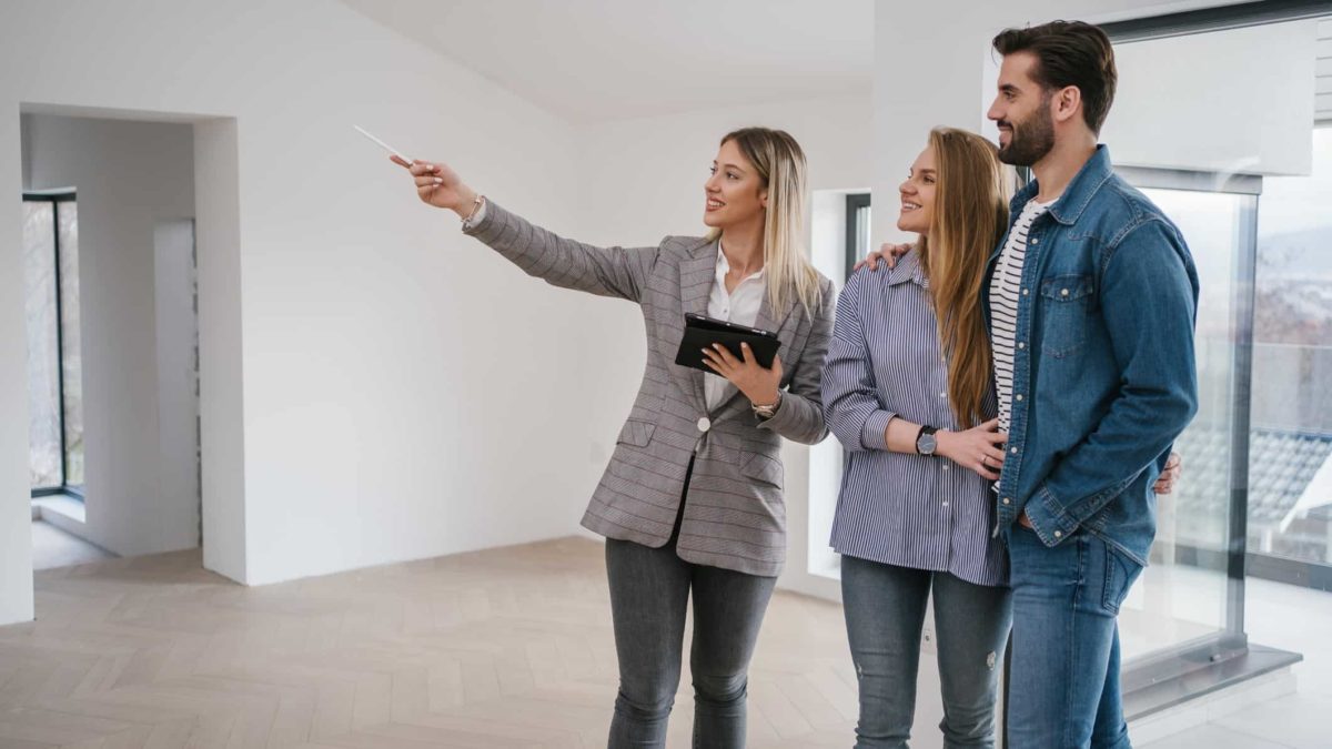 A young couple stands next to a real estate agent in an empty apartment they are inspecting