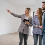 A young couple stands next to a real estate agent in an empty apartment they are inspecting