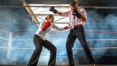 A woman in a business suit and a man in a business suit boxing in a ring.