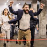 Man in an office celebrates at he crosses a finish line before his colleagues.