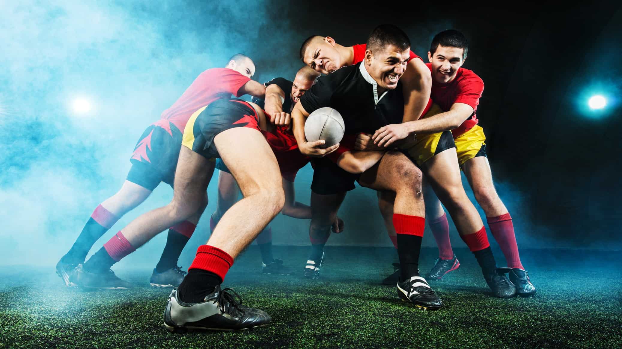 Rugby player runs with the ball as four tacklers try to stop him.