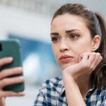 Close up of a sad young woman reading about declining share price on her phone.