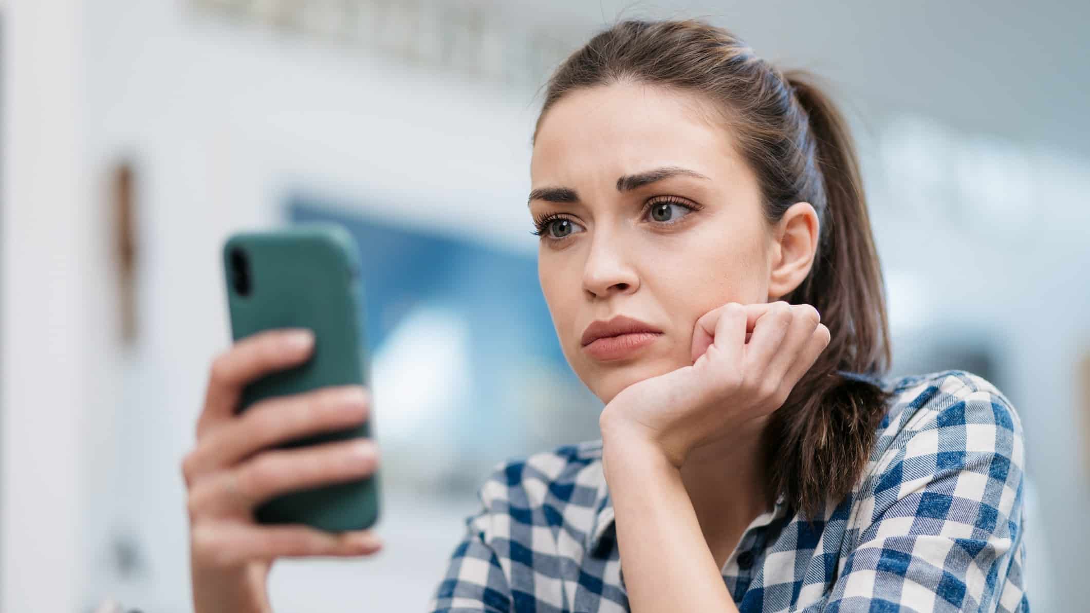 Close up of a sad young woman reading about declining share price on her phone.