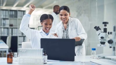 Two scientists in a Rhythm Biosciences lab cheer while looking at results on a computer.