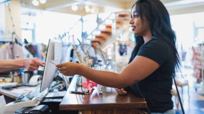 A young woman in a shop hands her credit card to the cashier