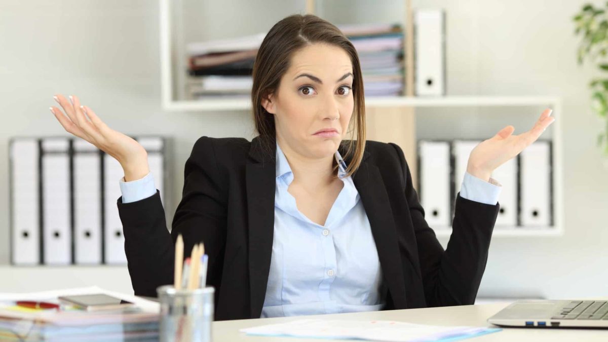 Woman sitting at a desk shrugs.