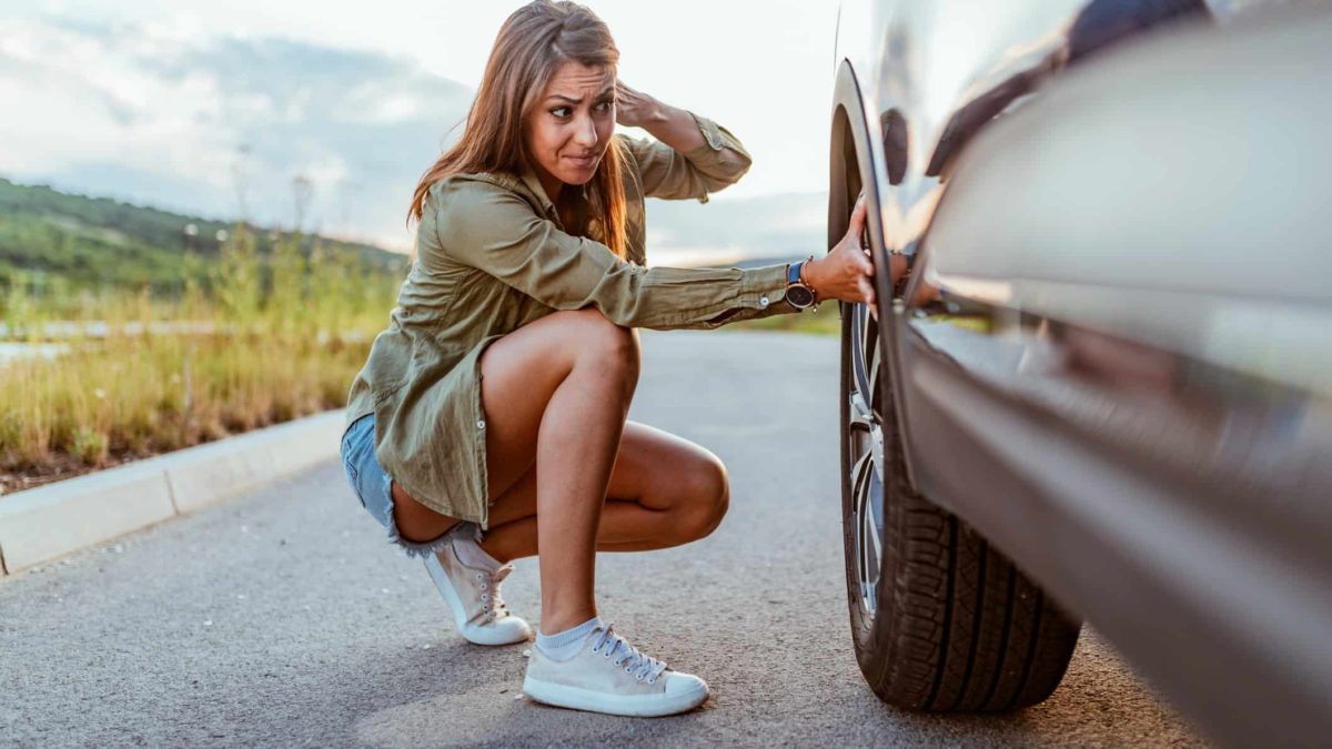 A woman stops on a road to check the tyre or wheel on her car