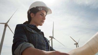 Female engineer holds plans at wind farm.