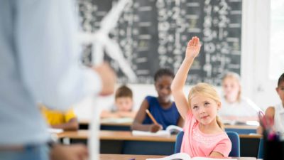 A teacher is standing up front of the classroom and is teaching his elementary students about wind turbines and alternative energy sources..