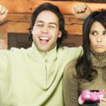 A man cheers after winning computer game while woman sitting next to him looks upset.