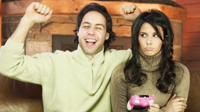 A man cheers after winning computer game while woman sitting next to him looks upset.