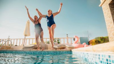 Two elderly retired women jump into a pool together laughing.