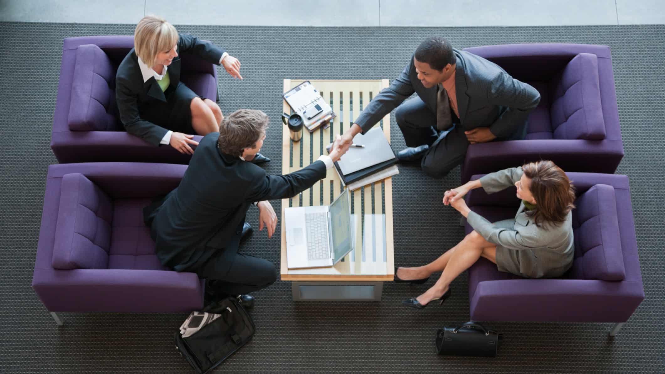 A group of business executives shake hands in an airport lounge.