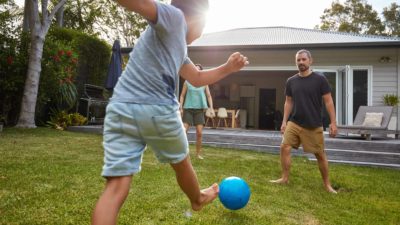 A boy boots the ball past his parents in a game of backyard soccer.