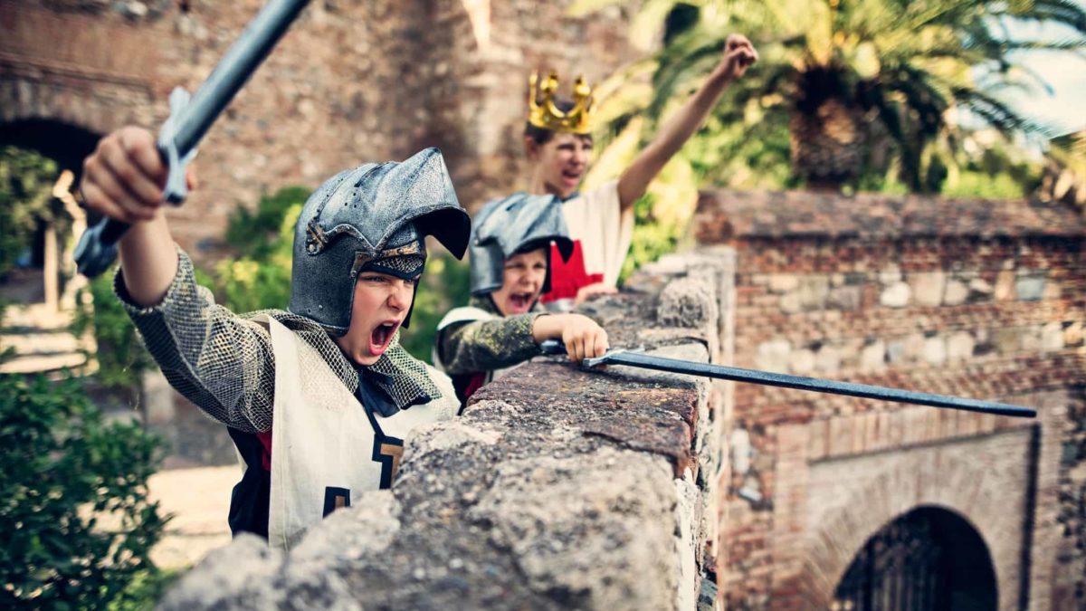 Three boys dressed as knights wield swords as they defend their castle wall.