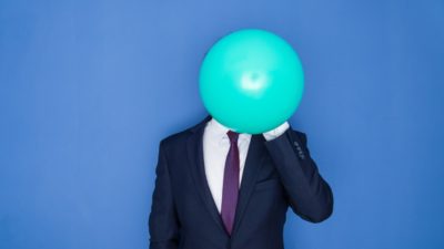 A business person holds a big balloon in front of their face.