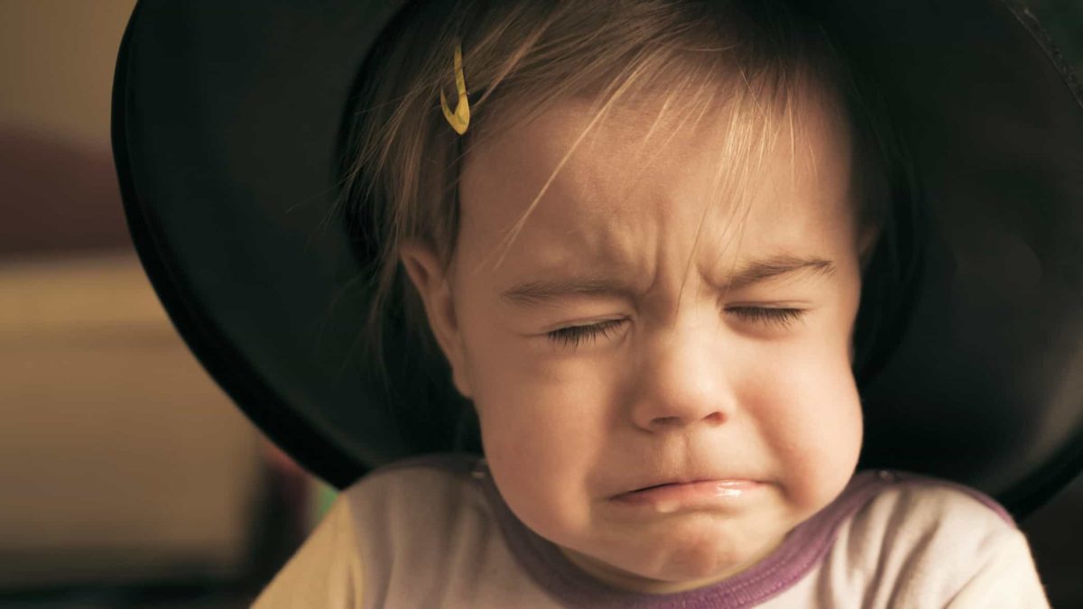 A little girl wearing a gold clip scrunches her face up about to cry.
