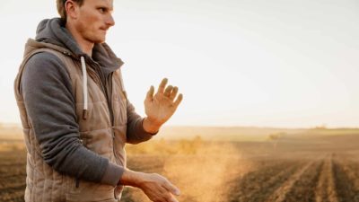 A farmer dusts the dirt off his hands in a field.