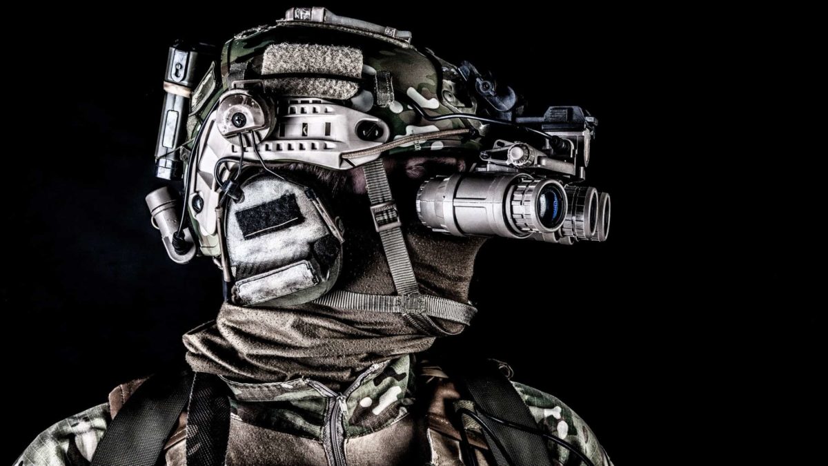 a soldier in combat gear wears electric optic equipment over his helmet.