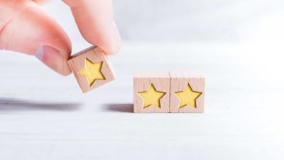 a forefinger and thumb hold a small block with a yellow star on it which is being placed next to two of the same blocks so they form a line of three blocks.