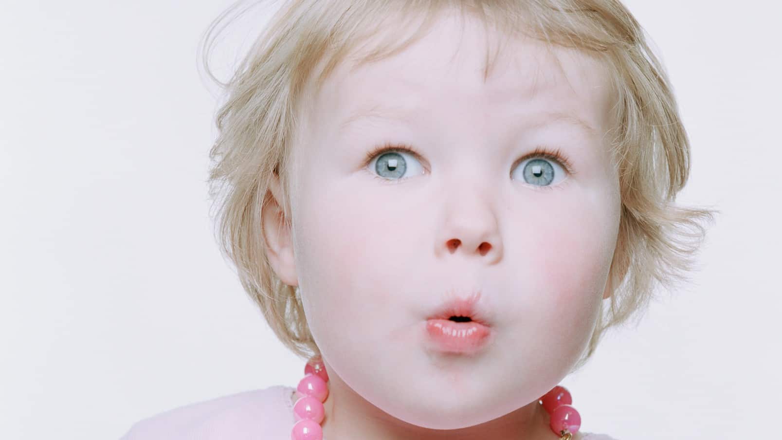 a young girl has a wide eyed look with pursed lips as though saying 'ooh' as if receiving interesting news or a juicy piece of gossip.