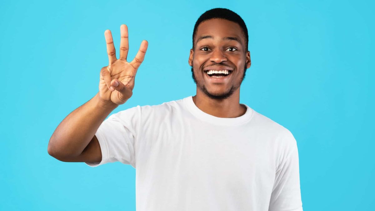 a man with a wide, eager smile on his face holds up three fingers.