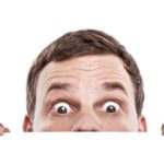 Half a man's face from the nose up peers over a table.