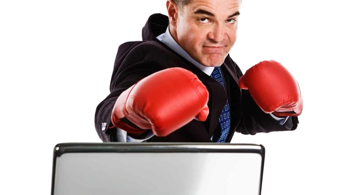 a man in a business suit wearing boxing gloves strikes a boxing pose with glove thrust forward atop a computer screen