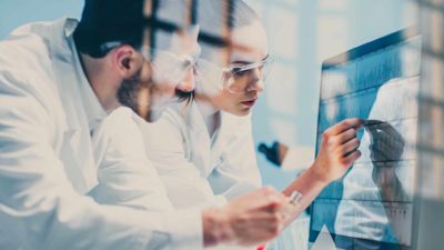 Two medical researchers in white coats collaborate over a computer screen of data in a medical research laboratory.