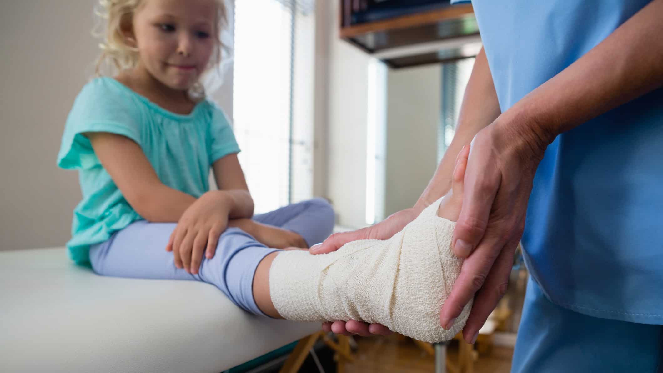 a doctor's hands take the bandaged foot and lower leg of a young girl in assessing treatment.